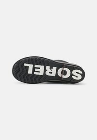 Suela de zapatilla de goma negra con un patrón de agarre texturizado; presenta el logo en blanco "SOREL" en el costado.