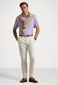 Ανδρικό σύνολο που περιλαμβάνει πουλόβερ πόλο με ανοιχτό μωβ ρίγες, μπεζ πουλόβερ δεμένο στους ώμους, κρεμ παντελόνια και καφέ μοκασίνια.