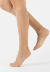 Calze a rete beige fino al ginocchio con texture morbida e fascia elastica in cima, progettate per adattarsi perfettamente alla gamba.