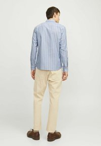 Šviesiai mėlynos juostelės marškiniai su ilgomis rankovėmis, derinami su grietinėlės spalvos kelnių ir rudo odiniu batų. Marškiniai turi klasikį apykaklę ir mygtukais užsegamus manžetus.