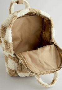 Sac à dos en tartan brun et crème avec un matériau extérieur en peluche, fermeture éclair, doublure beige et petite poignée de transport.