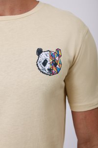 Bež majica od pamuka s grafikom panda glave, pola realistična, pola geometrijska u vibrantnim bojama uključujući plavu, ružičastu i žutu.