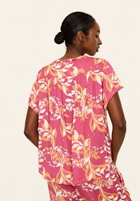 Blusa floreale a maniche corte, con una base rosa, motivi floreali arancioni e bianchi, tessuto leggero e dettagli plissettati sul retro.