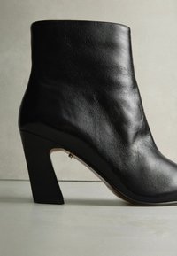Zwarte leren enkelboot met een slank ontwerp, gladde textuur en een geometrische hak. De boot heeft een getailleerde silhouette met minimale accenten.