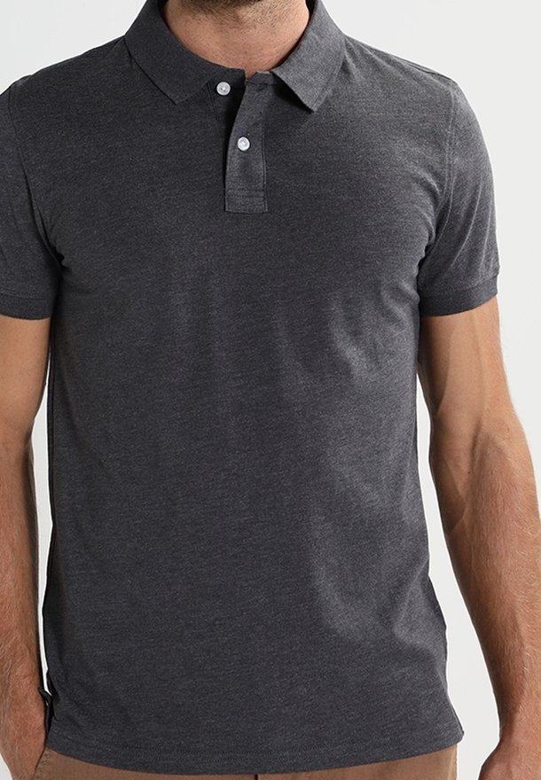 Homme portant un polo gris foncé ajusté à manches courtes avec deux boutons blancs et un col, debout devant un fond uni.