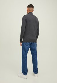 Suéter gris con un cuello alto y puños acanalados, combinado con jeans azules y zapatillas blancas, visto desde la parte de atrás. Diseño simple y casual.