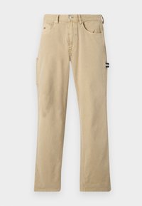 Beige Baumwollhose mit geraden Beinen, ausgestattet mit vorderen und seitlichen Taschen sowie einem kleinen marineblauen und weißen Logo-Patch an der Seite.