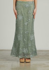 Groene gehaakte maxi-skirt met bloemenpatroon. Lichtgewicht, losvallend ontwerp en uitlopende zoom. Gepaard met geweven platform sandalen.