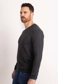 Maglione V-neck grigio scuro realizzato in materiale morbido, con maniche lunghe e design aderente. L'orlo presenta un sottile accento con logo.