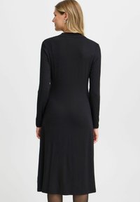 Mustan pitkän hihan mekko, jossa on virtaava siluetti, polvitaipeeseen ulottuva pituus, valmistettu pehmeästä ja sileästä kankaasta, jossa on yksinkertainen ja klassinen muotoilu.
