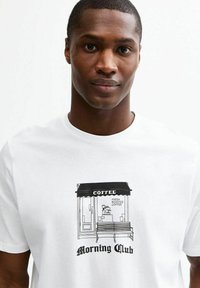 Camiseta blanca con un diseño gráfico negro de una cafetería, con el texto "Morning Club" y "Café Frescamente Tostado" debajo.