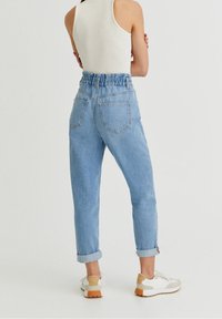 Light blue denim jeans with a high, gathered waistband, rolled cuffs, and two back pockets. Worn with white and beige sneakers.