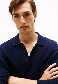 Polo de color azul marino en un tejido texturizado, con un collar clásico y tapeta de dos botones. Detalle del logo pequeño en el lado izquierdo del pecho.