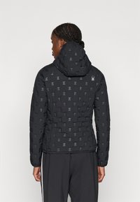 Jachetă neagră căptușită cu un model texturat, dotată cu glugă și un logo subtil pe spate. Materialul pare neted și ușor.