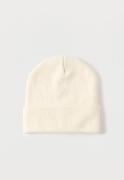 Πλεκτό σκουφάκι σε κρεμ απόχρωση με διπλωμένη μπάσκα, τοποθετημένο επίπεδα σε ανοιχτό γκρι φόντο.