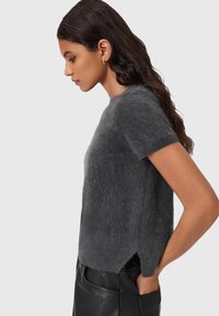 Korte ærmer, grå sweater lavet af blødt, fuzzy materiale med sideslids, båret over sorte læderbukser. Simpel, afslappet pasform.