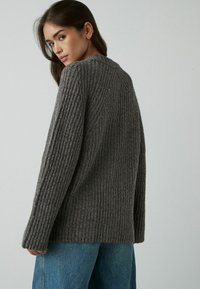 Suéter gris acanalado de manga larga, con un corte relajado y una textura suave. Combinado con unos pantalones vaqueros de talle alto en azul claro.