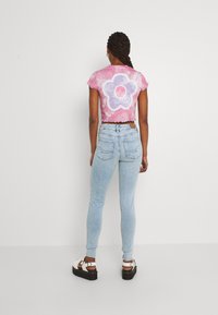 Kuttet rosa tie-dye t-skjorte med et lilla blomstermønster, kombinert med falmede blå skinny jeans og platåsandaler med hvite detaljer.