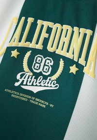 Camiseta deportiva verde y blanca con "CALIFORNIA" y "Athletic" en amarillo y blanco, con un acabado texturizado y acentos decorativos.