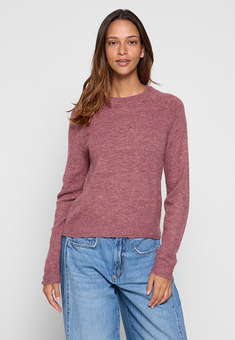 Maglione lavorato a maglia color rosa con scollo rotondo e maniche lunghe, caratterizzato da una texture morbida e un fit rilassato. Abbinato a jeans blu chiaro.
