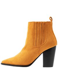 Bottine en daim jaune avec un bout pointu, des coutures verticales sur les côtés et un talon noir épais. Texture lisse et design élégant.