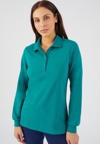 Camisa de polo de manga larga color teal con cuello abotonado, que presenta una textura suave y un ajuste relajado. Los botones visibles al frente añaden detalle.