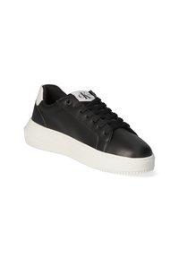 Sneaker in pelle nera con suola in gomma bianca, dotato di lacci neri, un logo sulla linguetta e un inserto sul tallone di colore bianco a contrasto.