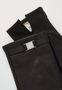 Sorte lærhansker med et rektangulært sølvfarget spenne, utskåret design ved håndleddet, og myk innvendig fôr for komfort.