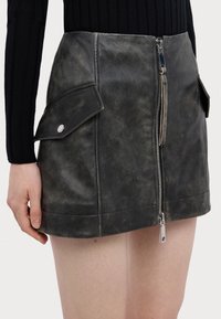 Gonna mini in pelle nera con zip frontale, due tasche laterali e una finitura testurizzata. Presenta accenti in hardware argentato.