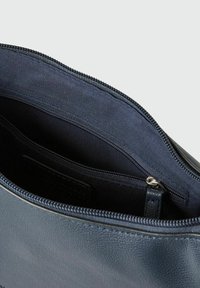 Interior de un bolso de cuero azul marino con un acabado texturizado. Cuenta con un bolsillo con cremallera y un forro de tela suave. Bordes de la cremallera visibles.