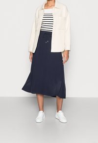 Navy midi skirt paired with a cream ribbed button-up jacket and black-and-white striped top, complemented by white sneakers.