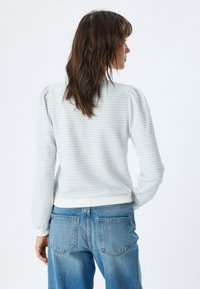 Lichtblauwe gebreide trui met textuur en pofmouwen, met ribgebreide manchetten en onderkant, gecombineerd met hoge taille denim jeans.