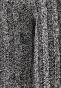 Tessuto lavorato a maglia grigio con strisce verticali in diverse sfumature di nero e grigio, dotato di una superficie texture e dettagli sottili.