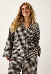 Czarny i kremowy zestaw piżamowy w kratkę składający się z dwóch części: koszuli zapinanej na guziki oraz spodni z szerokimi nogawkami, z luźnymi rękawami i kieszeniami po bokach.