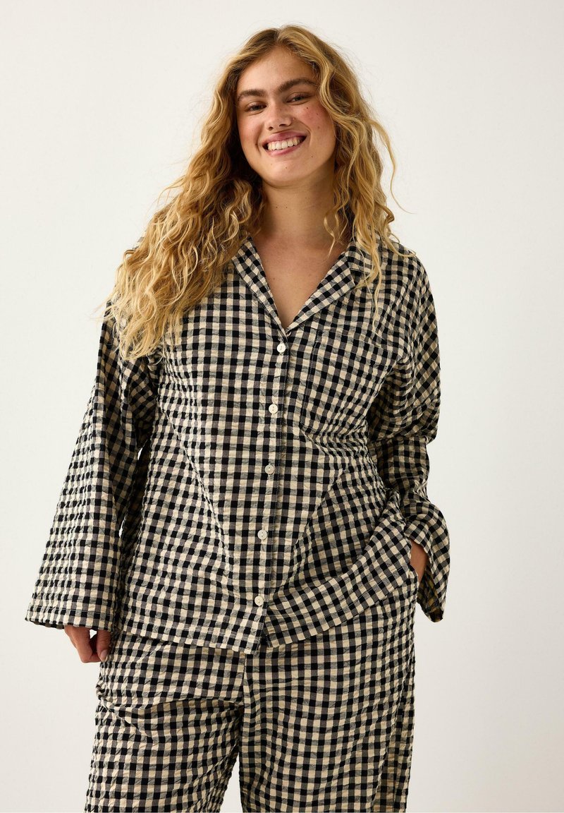 Czarny i kremowy zestaw piżamowy w kratkę składający się z dwóch części: koszuli zapinanej na guziki oraz spodni z szerokimi nogawkami, z luźnymi rękawami i kieszeniami po bokach.