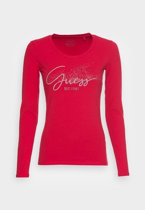 T-shirt rouge à manches longues avec col rond, inscription argentée "Guess EST. 1981" et motif de points scintillants sur la poitrine.