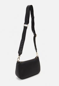 Svart läderhandväska med en texturerad yta, guldfärgad detaljer och en avtagbar rem med präglad logotyp. Kompakt, rektangulär form.