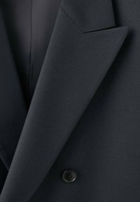 Tela de blazer azul marino oscuro con una textura suave, diseño de solapa afilada y un solo botón negro como detalle. Vista en primer plano que revela los detalles de la costura.