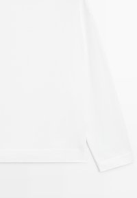 Hvid langærmet skjorte med rund halsudskæring, vist fra midthøjden til ærmet udgang mod en helt hvid baggrund.