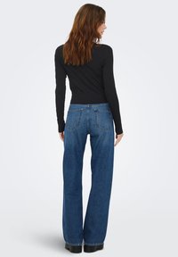 Blå jeans i den brede ben-model med høj talje, der har baglommer og kontrastsyning. Kombineret med en tætsiddende sort langærmet top.