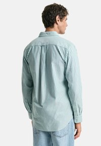 Camisa de manga larga a rayas verdes y blancas, hecha de algodón. Presenta un cuello, puños abotonados y un detalle en forma de pieza en la parte posterior.
