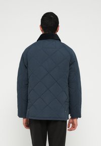 Μπλε σκούρο καπιτονέ μπουφάν με γιακά από κορντόνι, με κουτί σχήμα και ορατό ραφές. Τελειώνει λίγο πάνω από τη μέση.