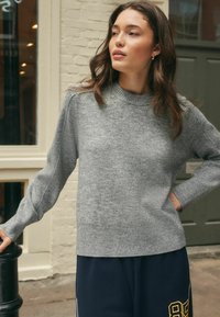 Grijze gebreide trui met een geribbelde kraag en manchetten, met een zachte textuur. Gerged gedragen met donkere broeken, wat een casual outfit accentueert.