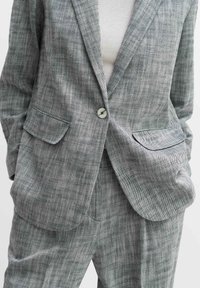Grijze, gestructureerde pak met een notch revers, twee voorzakken en een enkele knoopsluiting. Lichte stof met subtiele ruiten.