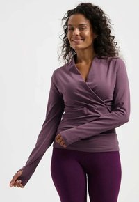 Langärmliges Oberteil in gedämpftem Lila, mit einem V-Ausschnitt und Wickeldesign sowie figurnahem Schnitt. Strukturierter Stoff mit Daumenlochärmeln und glatter Oberflächenbeschaffenheit.