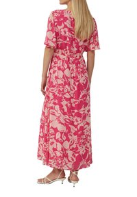 Robe maxi florale en rose et rose clair, avec des manches courtes, une taille smockée et une coupe fluide. Portée avec des sandales blanches à lanières.