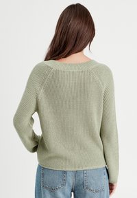 Pull en maille vert clair avec une texture côtelée, des manches raglan et un décolleté large, associé à un jean en denim bleu.