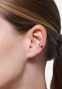 Ohrringe aus goldfarbenem Metall mit einer glatten, polierten Oberfläche, die ein schlankes Design und einen metallischen Glanz aufweisen und am Ohrläppchen getragen werden.