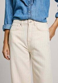 Jeans de cintura alta color crema con estampado de rayas, que cuentan con un cierre de botón, cinco bolsillos y un ajuste ligeramente relajado.