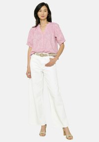 Rozā īsām piedurkēm izstrādāta blūze ar teksturētām dizaina detaļām, apvienota ar baltām platām biksēm un austu jostu. Modelis valkā sandales ar siksniņām.